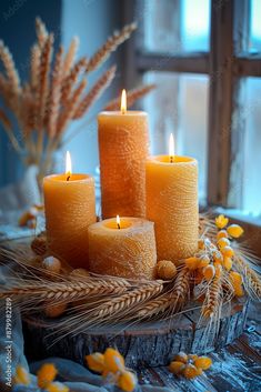 four lit candles sitting on top of a wooden table next to corn stalks and flowers