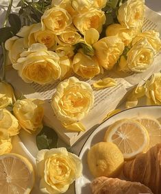 yellow roses and lemons are on the table with croissants in front of them