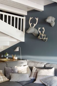 a living room filled with lots of furniture next to a stair case and wall mounted deer heads