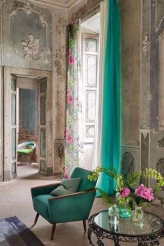 a green chair sitting in front of a window next to a table with flowers on it