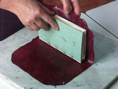 a person using a knife to cut something on a piece of red leather with a metal holder