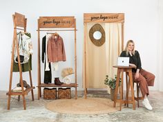 a woman sitting at a desk in front of two wooden clothes racks