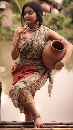 a woman carrying a large pot on her back while standing next to a body of water