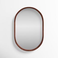 an oval mirror hanging on the wall next to a white wall with a wooden frame