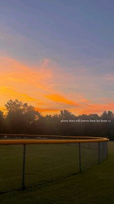 the sun is setting behind a chain link fence on a soccer field with trees in the background