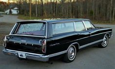 an old black station wagon parked on the side of the road in front of some trees