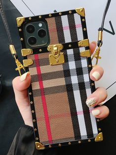 a woman is holding up her phone case with gold hardware and plaid pattern on it