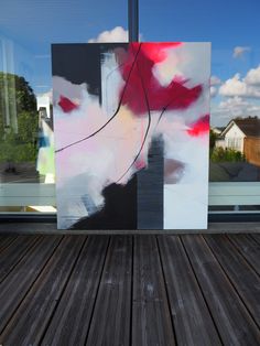 an abstract painting is displayed in front of a glass window with wood flooring on the outside