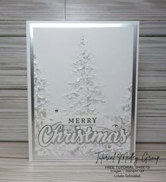 a white christmas card on a wooden surface with the words merry christmas written in silver