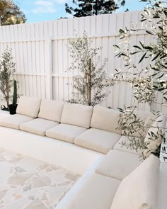 a white couch sitting next to a tall plant in a backyard area with stone flooring