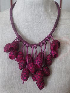 a pink and purple necklace on a mannequin's neck with red flowers