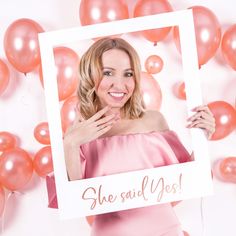 a woman in pink dress holding up a photo frame with balloons around her and she said yes