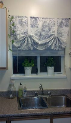 a kitchen sink under a window covered in curtains