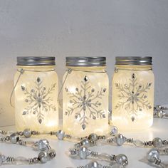 three mason jars with snowflakes on them are surrounded by beads and silver balls