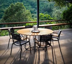 an outdoor table with four chairs and an umbrella on the deck overlooking trees in the distance