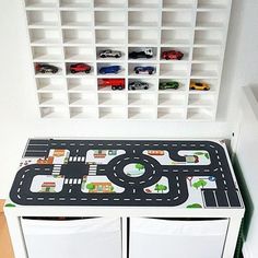 a toy table with cars and trucks on it in front of a white bookcase