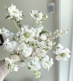 a vase filled with lots of white flowers on top of a table next to a window