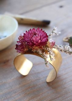 a pink flower in a brass cuff on a wooden table next to bowls and scissors