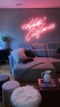 a living room filled with furniture and a neon sign on the wall above it that says hotel california