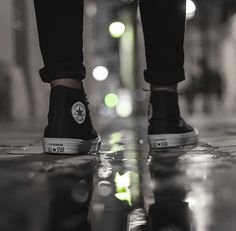 a person's feet in black and white sneakers on a wet floor with lights behind them