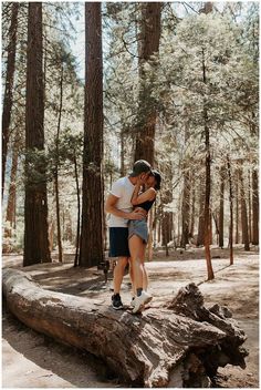 a man and woman standing on top of a log in the middle of a forest