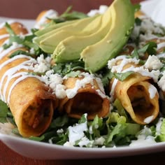 a white plate topped with meat and lettuce covered in sauces next to an avocado