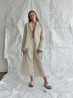 a woman standing in front of a white backdrop wearing a long jacket and wide pants