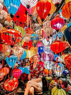 a woman sitting in front of many colorful lanterns