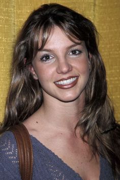 a woman with long brown hair and blue eyes smiling in front of a yellow curtain