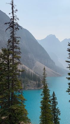 the mountains are covered with trees and blue water in the foreground is a lake surrounded by tall pine trees