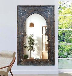 a mirror sitting on top of a white wall next to a chair and potted plant