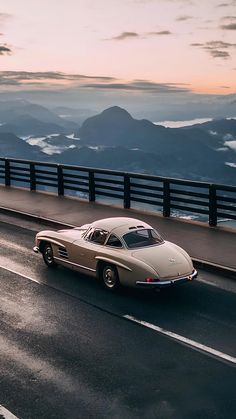 an old car driving down the road in front of some mountain range at sunset or dawn