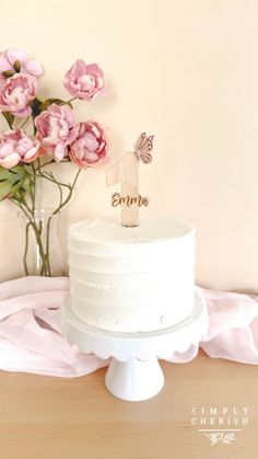 a white cake sitting on top of a table next to pink flowers and a wooden sign