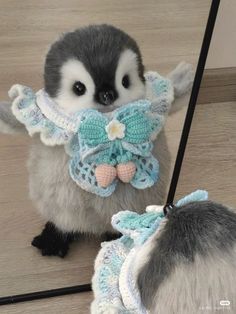 a small penguin with a crocheted bow around its neck is looking at itself in the mirror