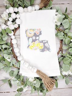 a white towel with a dog on it sitting next to some flowers and greenery