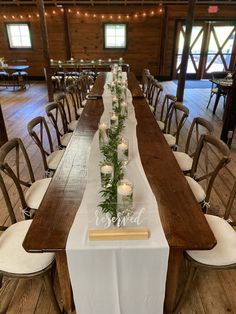 a long table with candles and greenery on it in a large room filled with wooden floors