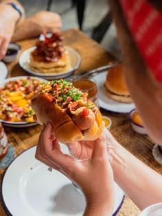 a person holding a hot dog in front of other people at a table full of food