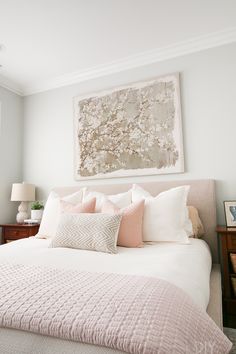 a bed with pink and white pillows in a bedroom next to a painting on the wall