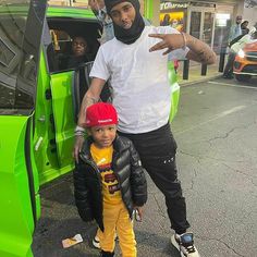 a man standing next to a little boy in front of a green car with his hand out