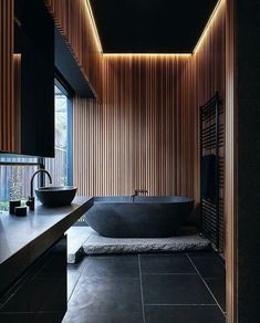 a black bathroom with wooden walls and flooring is lit by recessed lights above the bathtub