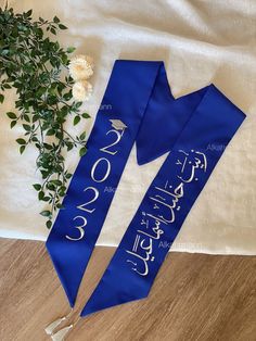 two blue sashs with arabic writing on them next to a white flower and cloth