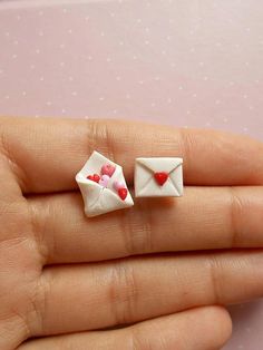 two tiny white envelopes with hearts are held in someone's hand