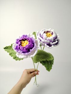 two crocheted flowers being held by a person's hand on a white background