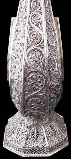 an ornate silver vase with intricate designs on the bottom and sides, set against a black background