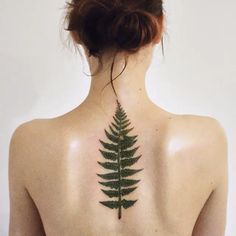 a woman with a tattoo on her back that has a green fern leaf on it