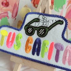 an embroidered sign that says, justaffit with sunglasses on it in front of colorful wallpaper