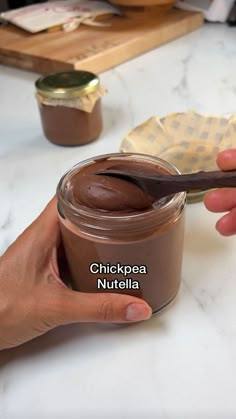 a person is holding a jar of nutella with a spoon in it on a table