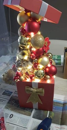 a christmas tree made out of boxes with lights and ornaments on it, sitting on top of newspapers