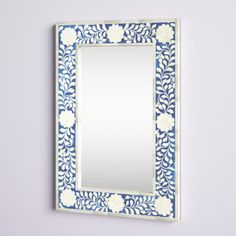 a blue and white mirror hanging on the wall next to a purple wall with flowers