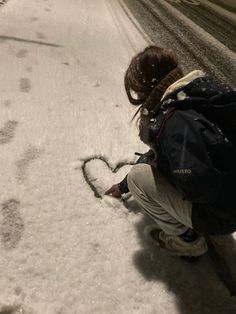 a woman kneeling down in the snow making a heart shape with her hands and writing on it